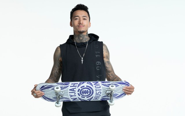 Nyjah Huston holding a skateboard against white backdrop. 